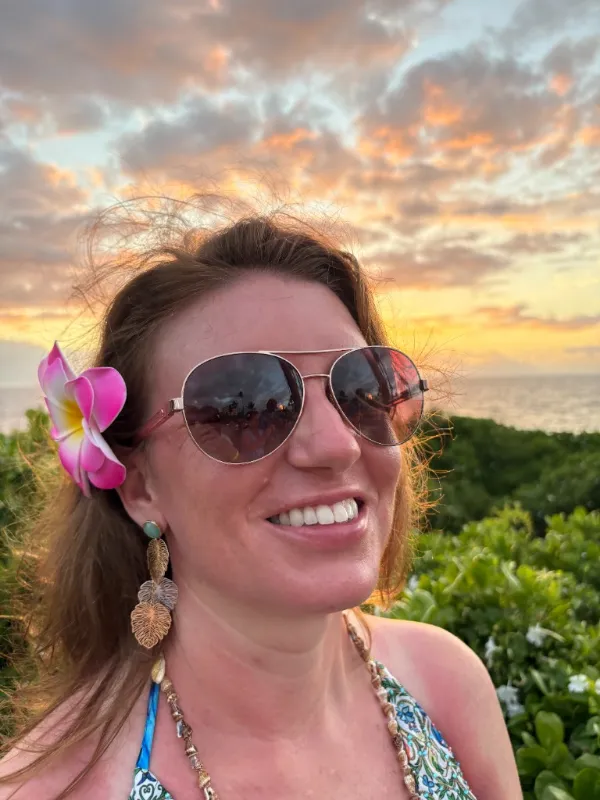 Sarah, the founder of Totes of Love, smiling with a pink flower in her hair and a sunset behind her.